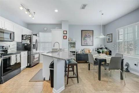 kitchen with stainless steel appliances, a kitchen island with sink, sink, white cabinetry, and hanging light fixtures