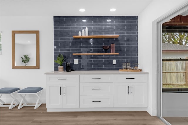 bar with light wood-type flooring, white cabinetry, and tasteful backsplash