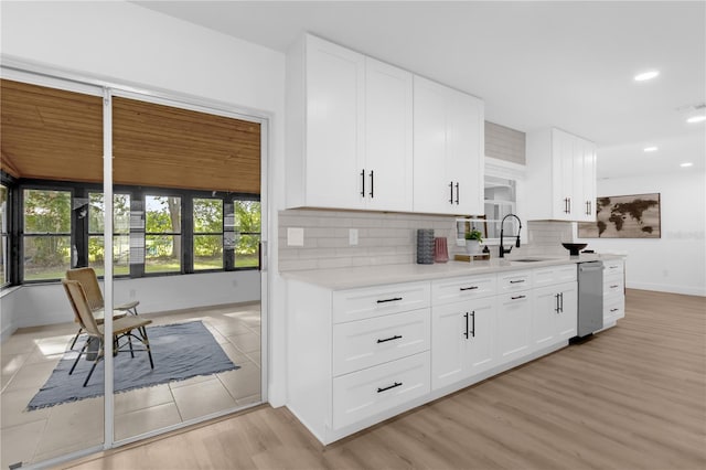 kitchen with white cabinets, sink, stainless steel dishwasher, decorative backsplash, and light wood-type flooring