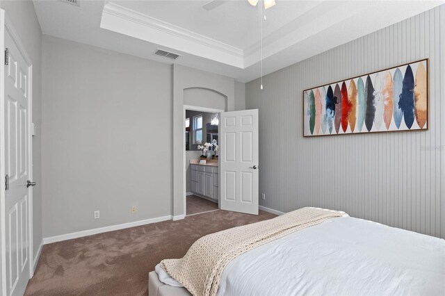 carpeted bedroom featuring ceiling fan, a raised ceiling, crown molding, and connected bathroom