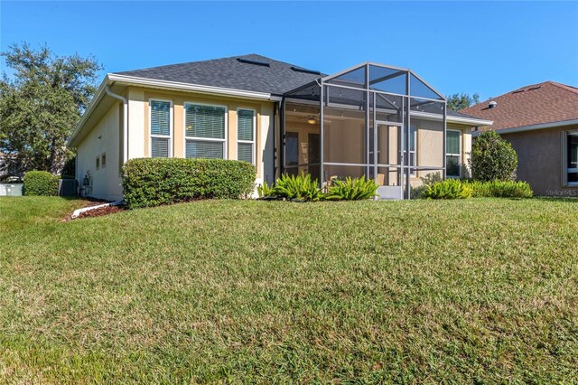 rear view of property with a lanai, a lawn, and central AC unit