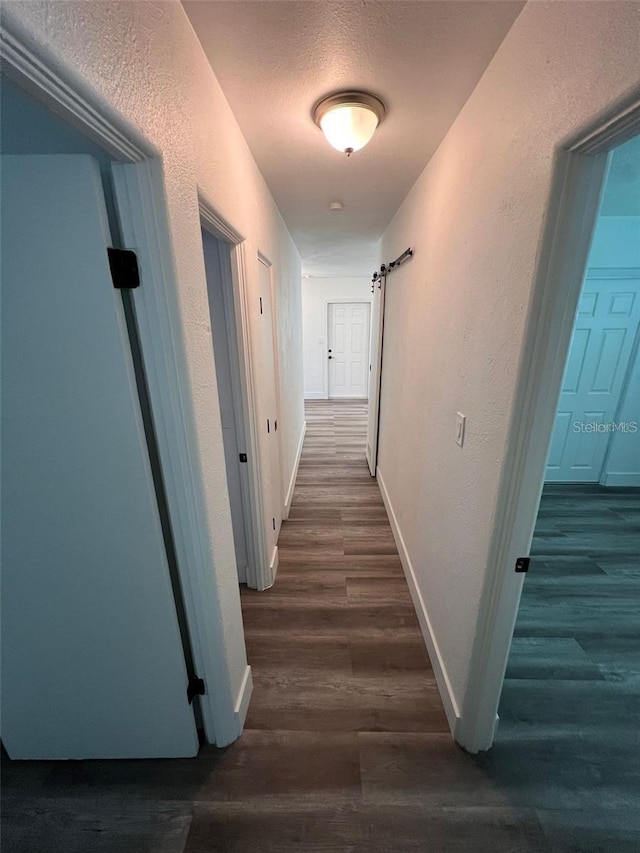 hallway featuring dark hardwood / wood-style flooring, a barn door, and a textured ceiling