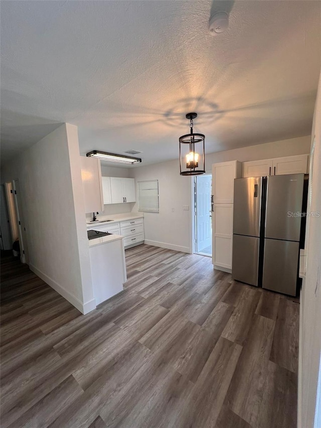 kitchen featuring white cabinets, wood-type flooring, stainless steel refrigerator, and pendant lighting