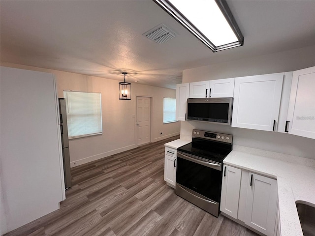 kitchen featuring stainless steel appliances, white cabinetry, hanging light fixtures, and hardwood / wood-style flooring