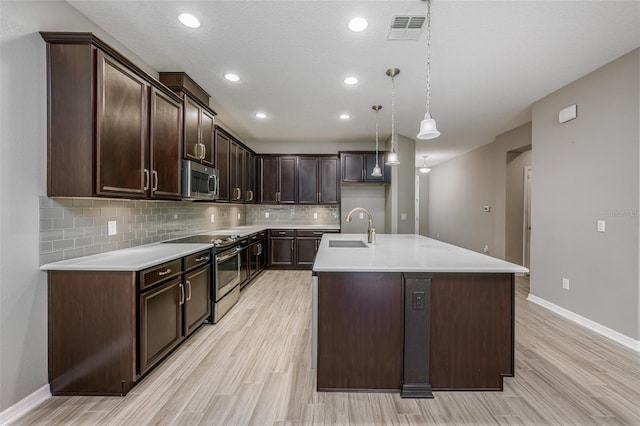 kitchen with dark brown cabinetry, a kitchen island with sink, sink, and appliances with stainless steel finishes