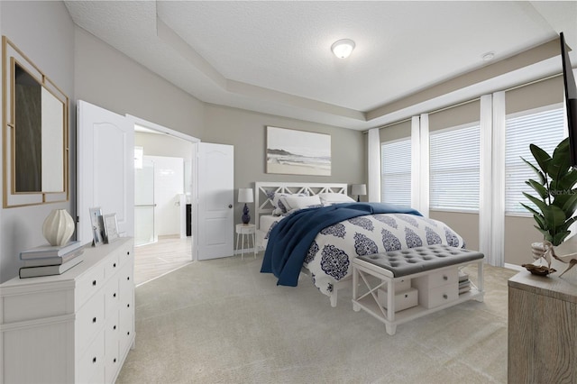 bedroom with light colored carpet, a textured ceiling, and a tray ceiling