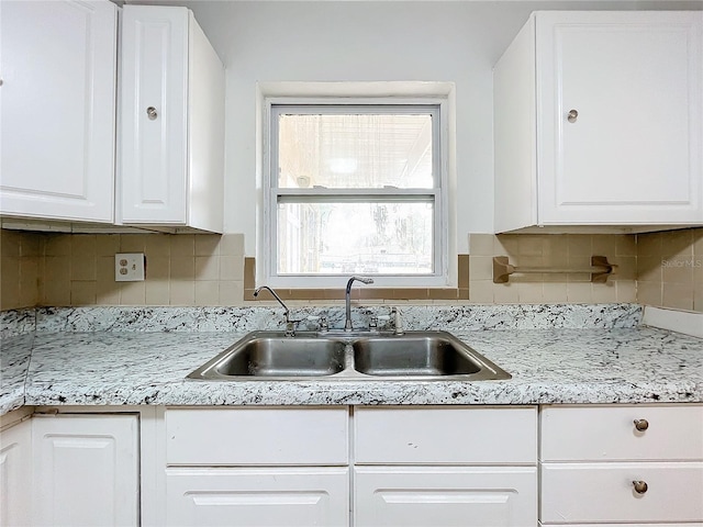 kitchen featuring white cabinetry, sink, light stone counters, and decorative backsplash