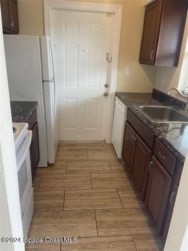 kitchen with white appliances, dark brown cabinetry, dark stone counters, and sink