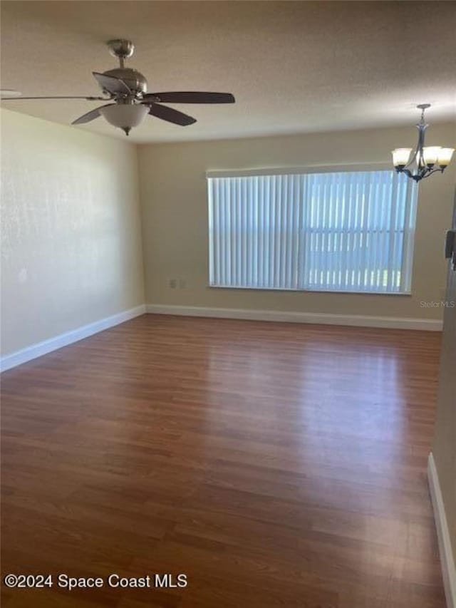 unfurnished room featuring ceiling fan with notable chandelier, dark hardwood / wood-style flooring, and a wealth of natural light