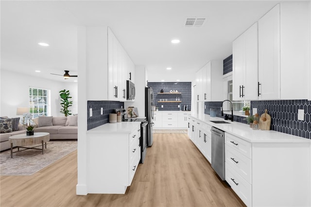 kitchen featuring light wood-type flooring, tasteful backsplash, stainless steel appliances, sink, and white cabinetry