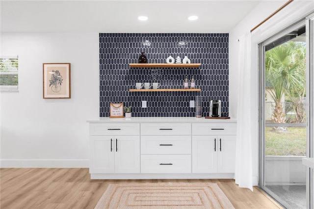 bar featuring white cabinets, decorative backsplash, and light hardwood / wood-style flooring