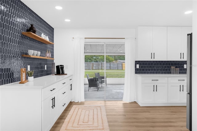 kitchen featuring white cabinets, light hardwood / wood-style floors, backsplash, and stainless steel refrigerator