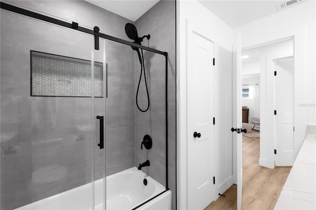 bathroom featuring hardwood / wood-style floors and bath / shower combo with glass door