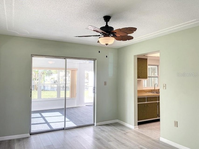 unfurnished room featuring ceiling fan, sink, a textured ceiling, and light wood-type flooring