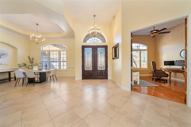 tiled entrance foyer with a tray ceiling, a wealth of natural light, french doors, and ceiling fan with notable chandelier