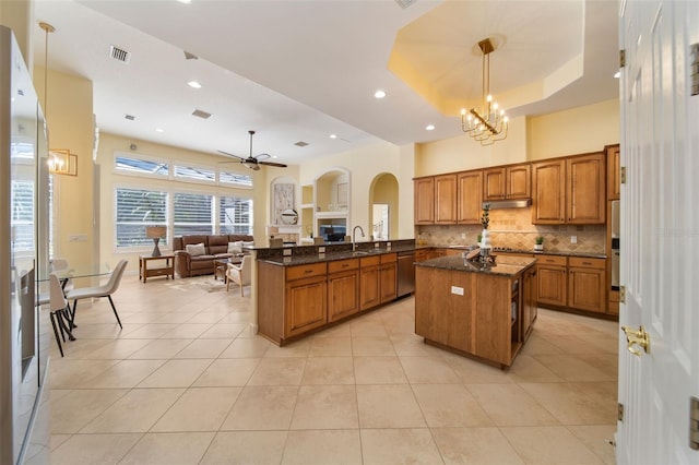 kitchen featuring sink, kitchen peninsula, dark stone countertops, decorative light fixtures, and ceiling fan with notable chandelier