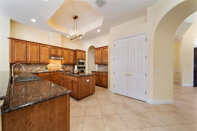 kitchen with pendant lighting, a center island, sink, appliances with stainless steel finishes, and a tray ceiling