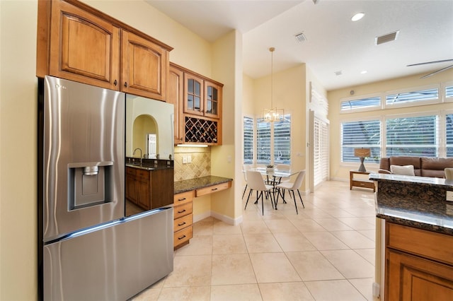 kitchen featuring decorative backsplash, stainless steel fridge, dark stone countertops, hanging light fixtures, and light tile patterned flooring