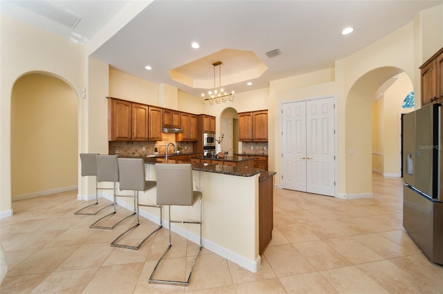 kitchen featuring a raised ceiling, decorative backsplash, dark stone countertops, a kitchen island, and stainless steel appliances