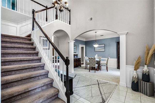 stairs featuring a high ceiling, tile patterned floors, ornamental molding, and ornate columns