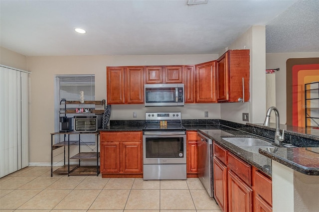 kitchen featuring kitchen peninsula, stainless steel appliances, light tile patterned floors, dark stone countertops, and sink