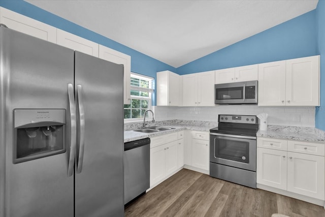 kitchen with decorative backsplash, white cabinetry, stainless steel appliances, and vaulted ceiling