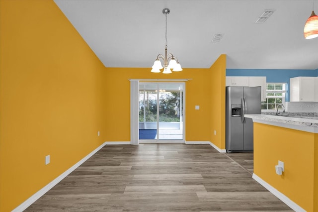 kitchen with a healthy amount of sunlight, hanging light fixtures, stainless steel fridge, a chandelier, and white cabinets