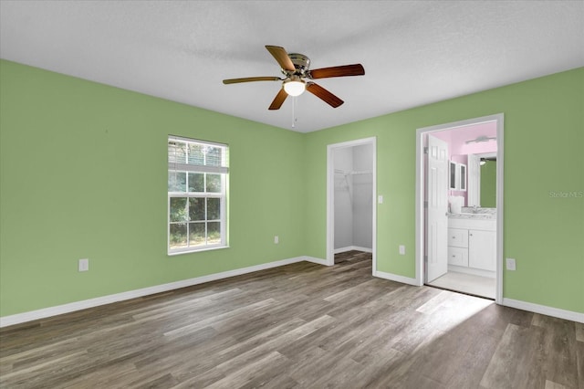 unfurnished bedroom featuring ensuite bath, hardwood / wood-style flooring, ceiling fan, a spacious closet, and a closet