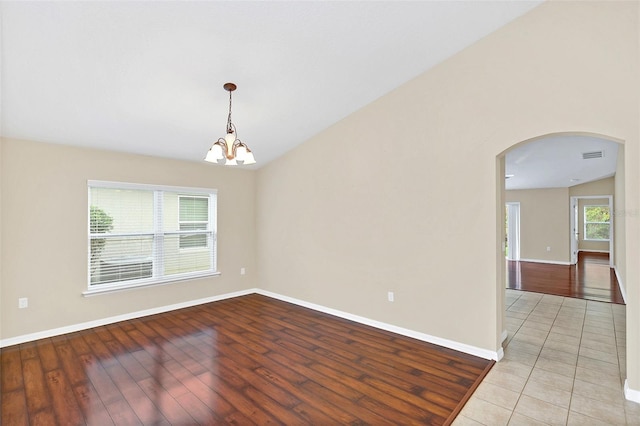 spare room featuring a chandelier, vaulted ceiling, and light wood-type flooring