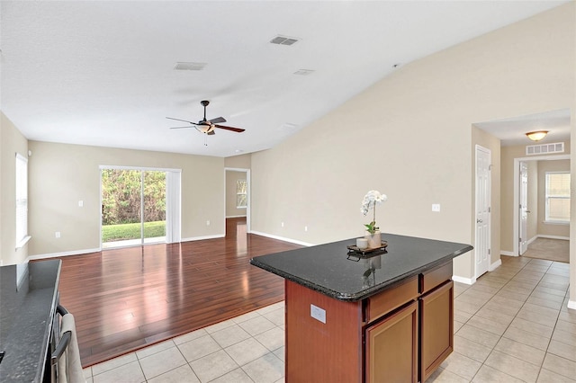 kitchen with light tile patterned floors, a center island, ceiling fan, and dark stone counters