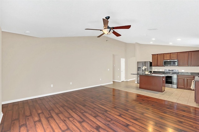 kitchen featuring vaulted ceiling, ceiling fan, light tile patterned floors, an island with sink, and stainless steel appliances