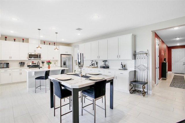 kitchen with a center island with sink, decorative backsplash, stainless steel appliances, and hanging light fixtures