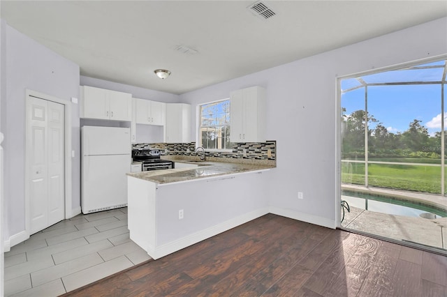 kitchen with kitchen peninsula, sink, electric stove, white fridge, and white cabinetry