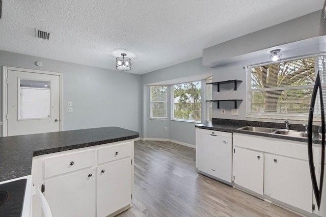 kitchen with white dishwasher, white cabinets, a textured ceiling, and a wealth of natural light