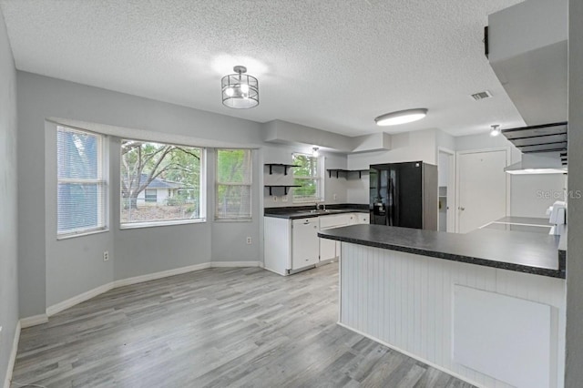 kitchen featuring black fridge, kitchen peninsula, a textured ceiling, light hardwood / wood-style floors, and white cabinetry