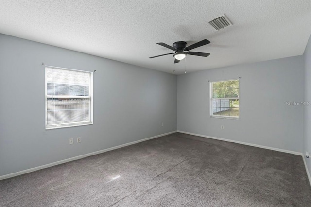 unfurnished room featuring ceiling fan, a healthy amount of sunlight, a textured ceiling, and dark carpet