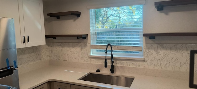 kitchen with decorative backsplash, stainless steel fridge, light stone counters, sink, and white cabinets