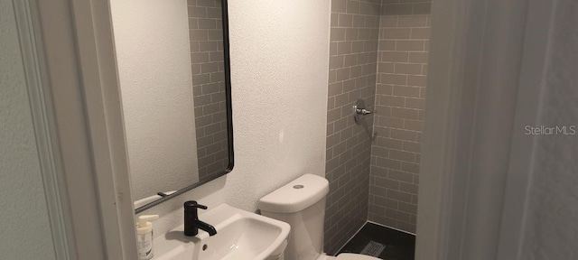 bathroom with toilet, a tile shower, and sink