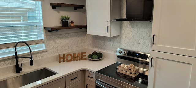 kitchen featuring stainless steel electric range oven, backsplash, wall chimney exhaust hood, white cabinets, and sink