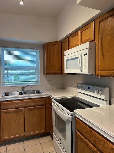 kitchen with brown cabinets, light countertops, light tile patterned flooring, a sink, and white appliances