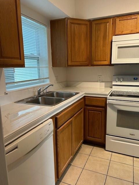 kitchen with light countertops, brown cabinetry, light tile patterned flooring, a sink, and white appliances