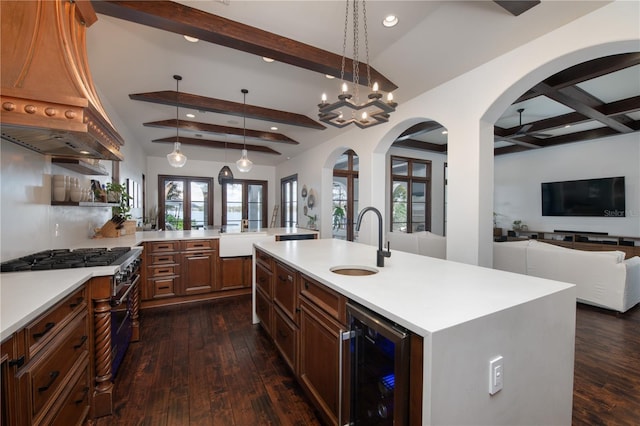 kitchen with sink, an island with sink, beamed ceiling, decorative light fixtures, and beverage cooler