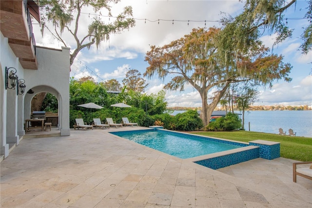 view of swimming pool featuring a yard, a water view, and a patio area