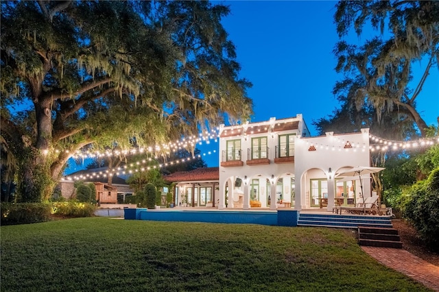 back house at night with french doors and a yard