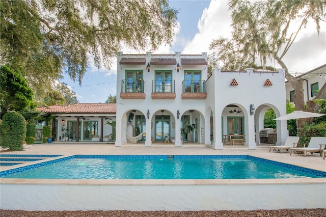 rear view of property with french doors, a balcony, ceiling fan, and a patio area