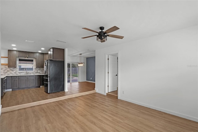 kitchen featuring backsplash, ceiling fan, light hardwood / wood-style floors, stainless steel refrigerator, and hanging light fixtures