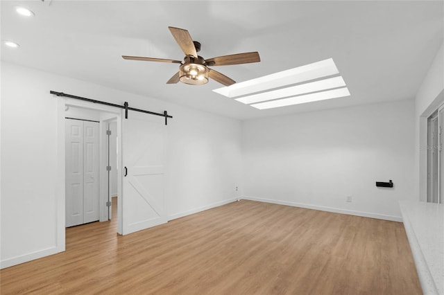 unfurnished room featuring light wood-type flooring, ceiling fan, and a barn door