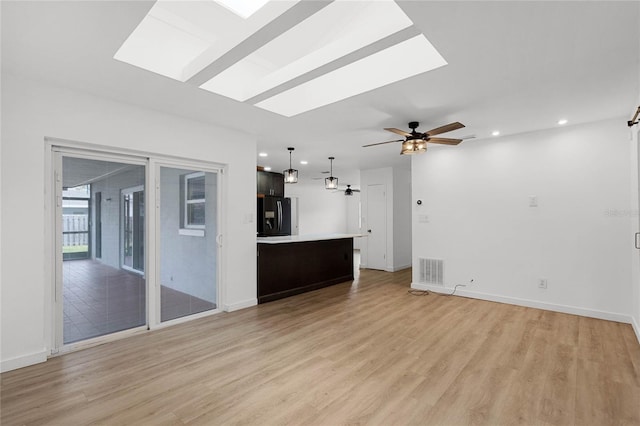 unfurnished living room featuring light wood-type flooring, a skylight, and ceiling fan