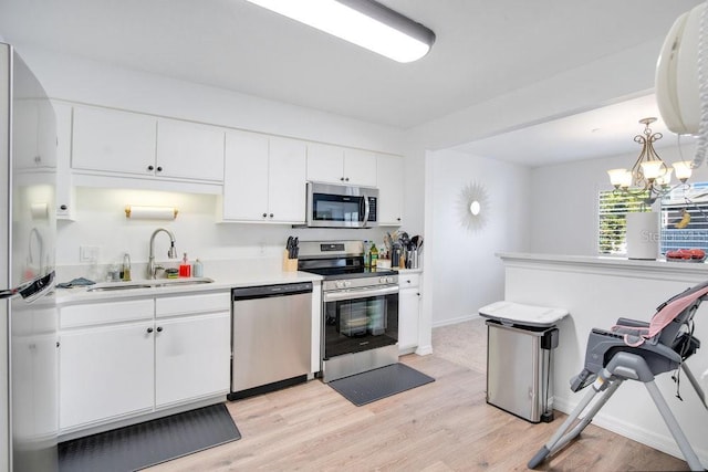 kitchen featuring sink, white cabinetry, hanging light fixtures, light hardwood / wood-style flooring, and appliances with stainless steel finishes