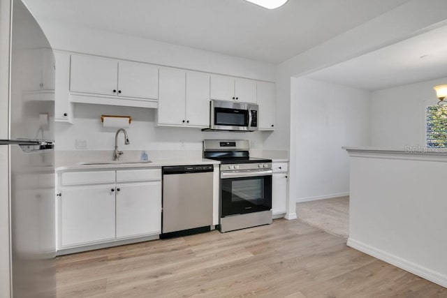 kitchen with white cabinets, light wood-style flooring, stainless steel appliances, light countertops, and a sink